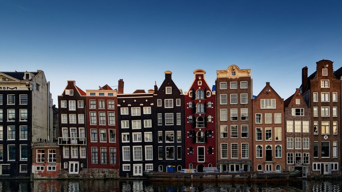 Amsterdam'da kanal kenarına dizilmiş renkli cepheli tarihi evler ve su yüzeyindeki yansımaları