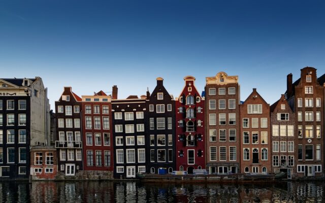Amsterdam'da kanal kenarına dizilmiş renkli cepheli tarihi evler ve su yüzeyindeki yansımaları