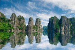 Ha Long Körfezi'nde turkuaz suyun üzerinde yükselen kireçtaşı adacıkları ve sakin bir tekne