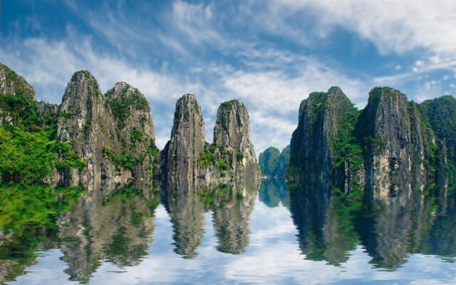 Ha Long Körfezi'nde turkuaz suyun üzerinde yükselen kireçtaşı adacıkları ve sakin bir tekne