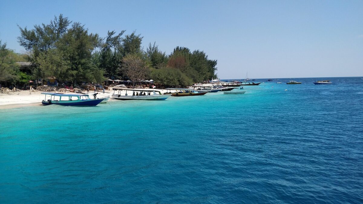 Lombok adasında Gili Trawangan sahilinde turkuaz denize uzanan açık renkli kumsal ve tekneler