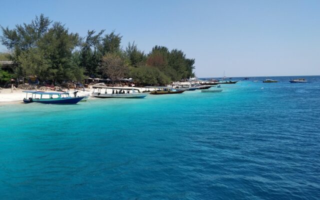 Lombok adasında Gili Trawangan sahilinde turkuaz denize uzanan açık renkli kumsal ve tekneler