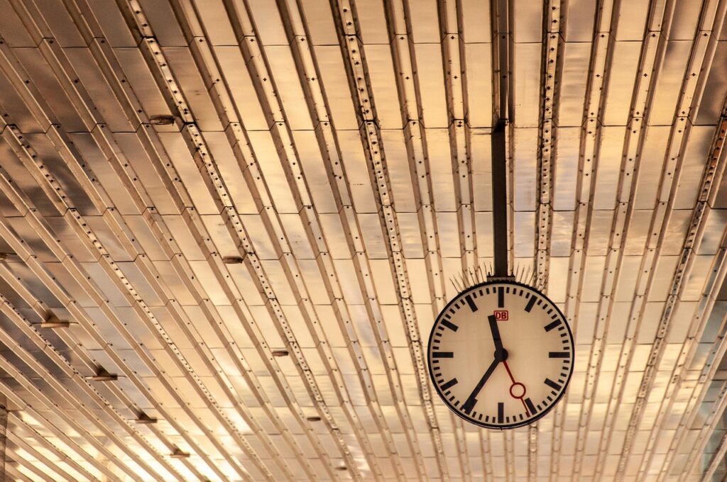Avrupa'da bir tren istasyonunda büyük saat ve bekleyen yolcular
